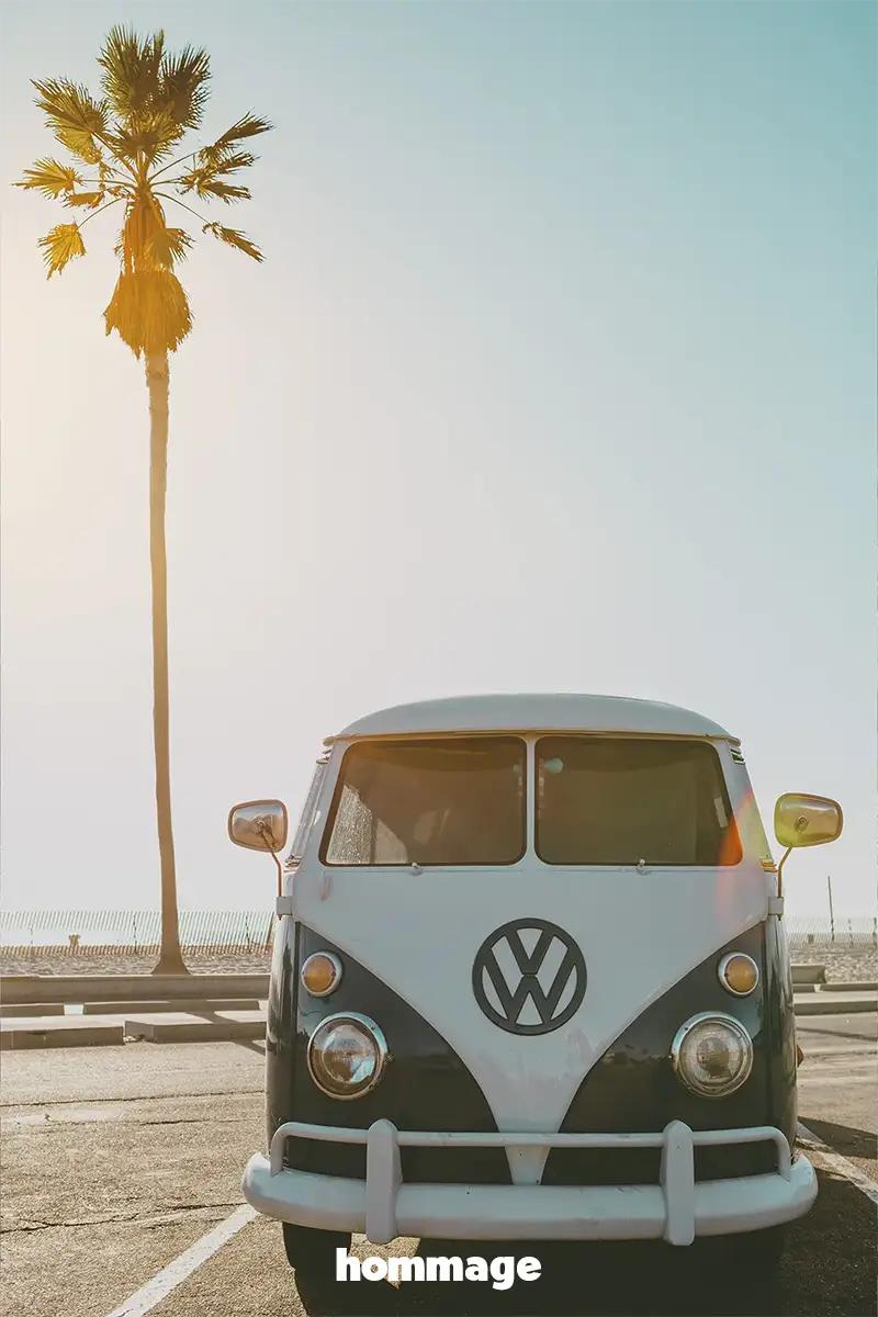 Vintage Volkswagen van under palm tree on sunny coast, embodying Hommage's spirit of travel and discovery.